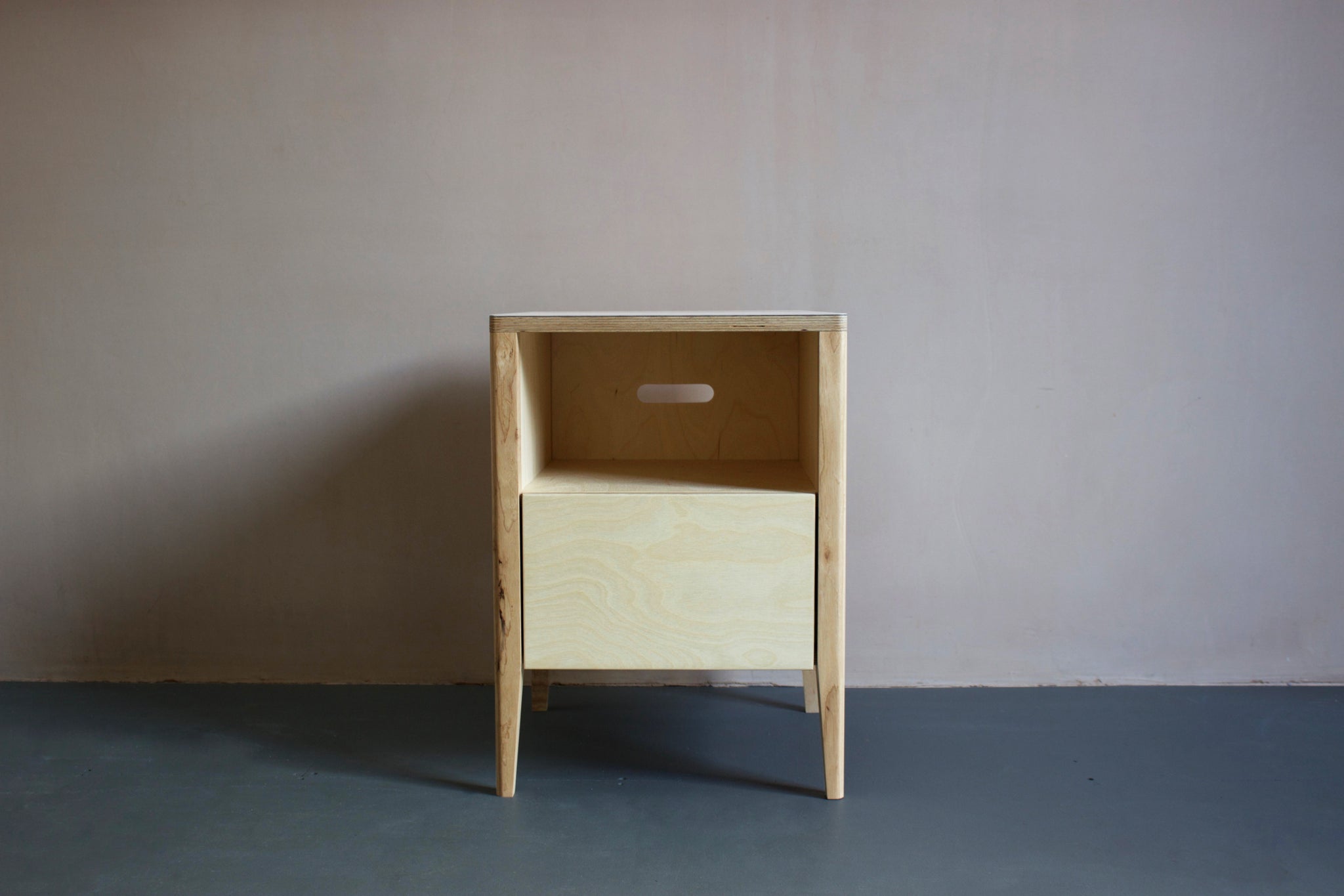 The Huxley bedside table in birch plywood, featuring solid ash legs and Forbo linoleum plywood top. Designed and made by Jon Grant London in Leyton, East London.