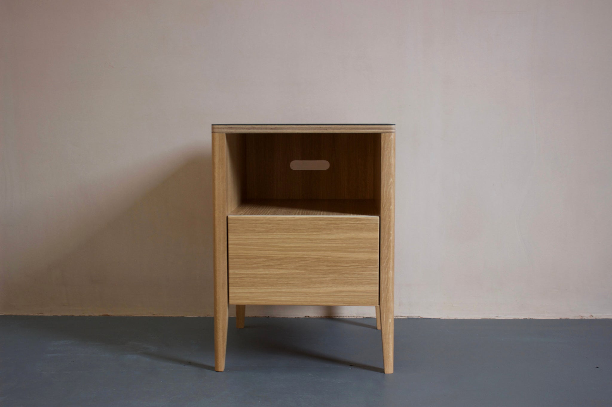 The Huxley bedside table in oak veneer plywood with Forbo linoleum top and solid oak legs. Designed and made by Jon Grant London in Leyton, East London.