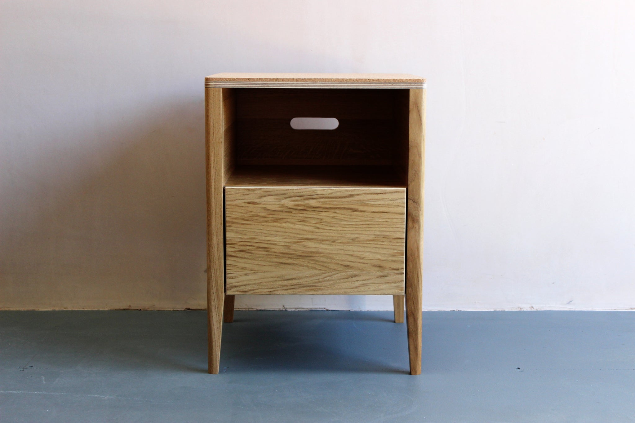 Handmade bedside table| cabinet, perfect for a modern home. It features cork top with oak veneered plywood and solid oak legs. Made by Jon Grant London in Leyton, East London.
